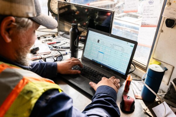 Person in safety vest uses laptop at a desk.