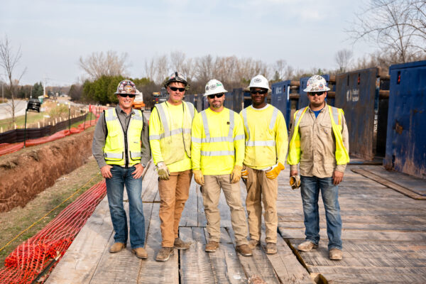 Five workers in safety gear stand on platform at worksite.