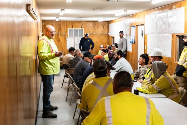 Workers in safety gear listen to a speaker at front.