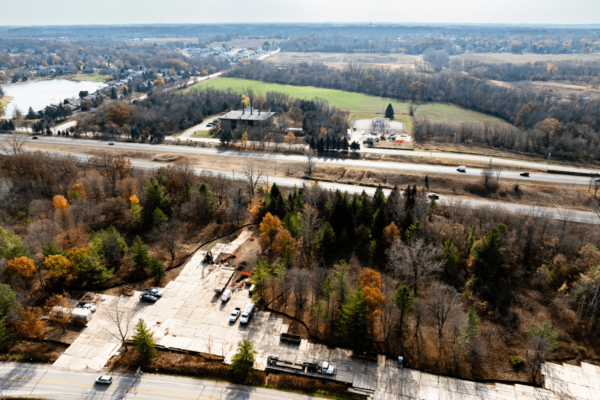 Aerial view: construction site by woods, highway, homes visible.