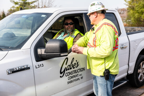 Two workers in safety gear talk in and beside Gabe's Construction truck.
