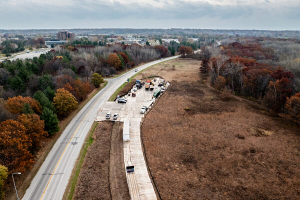 Aerial view: construction site by Wisconsin road, autumn trees, construction equipment visible.