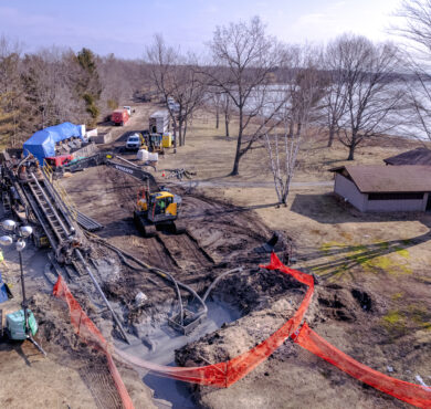 Horizontal directional drilling construction site with machinery, mud, barriers, lake, and bare trees at Dunes State Park