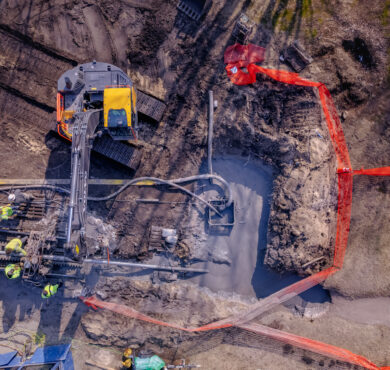 Aerial view of construction workers digging trench with machinery, fenced area.
