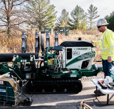 Worker operates pipe fusion machine roadside, tools and pipes nearby.