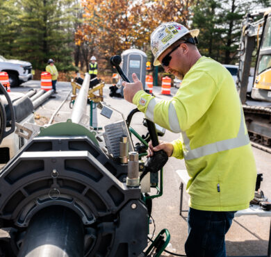 Worker in yellow gear operates horizontal directional drill at Green Bay, Wisconsin road site with cones.