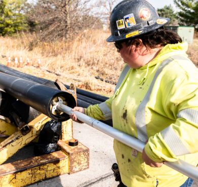 Worker in safety gear inserts metal rod into black pipe.