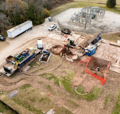 Aerial view: workers, machines, trucks near electrical substation, excavated soil.
