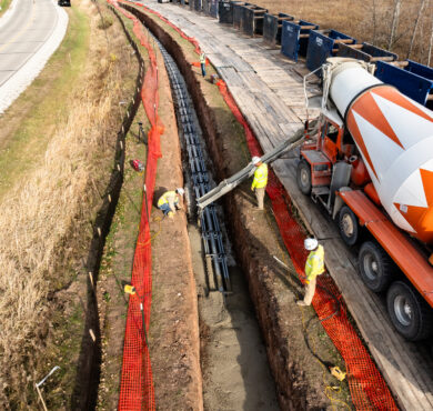 Aerial view: workers pour concrete into high-voltage utility trench beside rural road in Green Bay, Wisconsin.