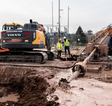 Two workers by drilling machinery in muddy construction site.