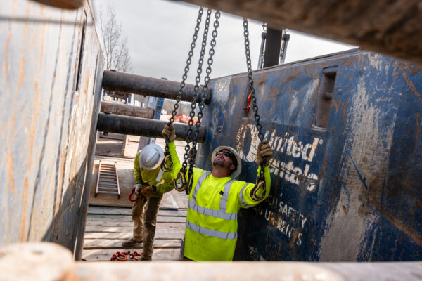 Two construction workers in safety gear adjust heavy chains at worksite in Green Bay, Wisconsin.
