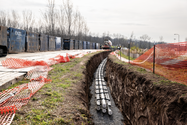 Utility cables in trench, orange fencing, equipment, cloudy day.