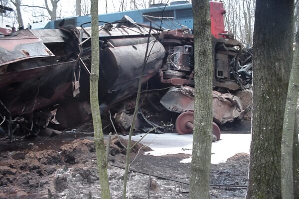 Derailed train engine lies damaged on its side among trees.