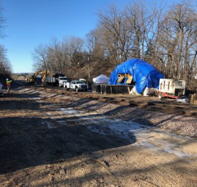 Utility vehicles and workers by railroad tracks with blue tarp.