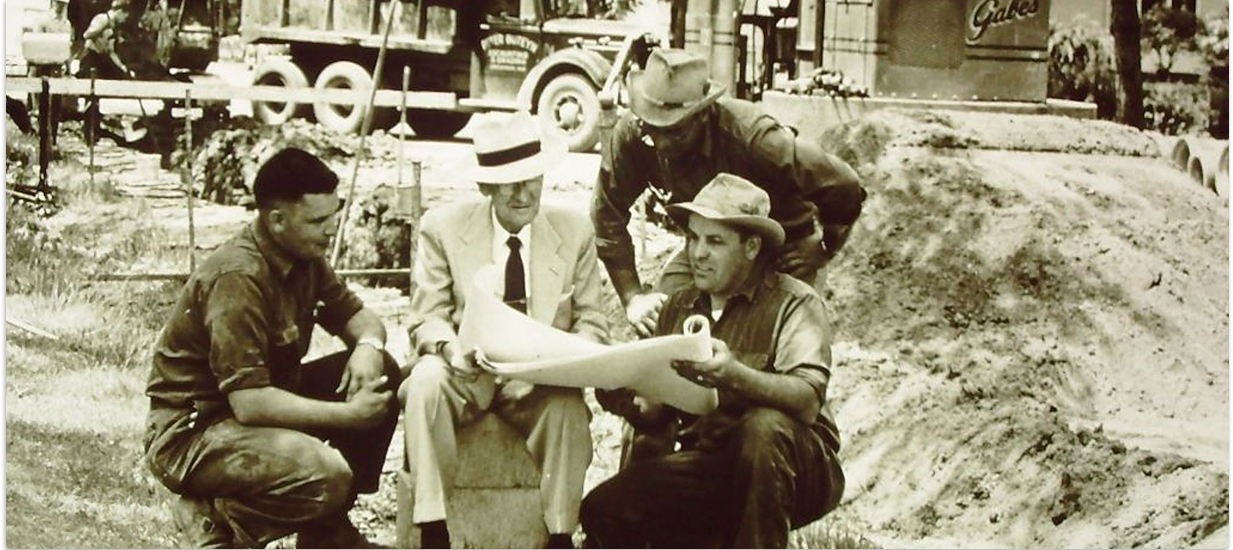 1954 photo showing four men from Gabe's reviewing plans at construction site with materials.