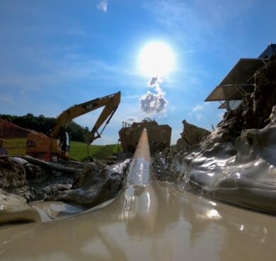 Excavator and muddy pipeline at sunny construction site in the wetlands.