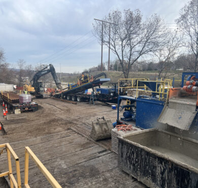 Construction site with machinery, barriers, cones; trees and clouds.